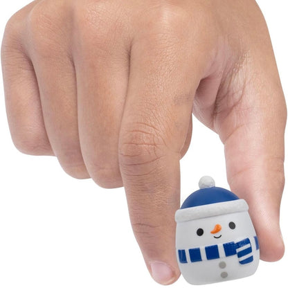 A small snowman figurine being held between a person's fingers against a plain white background.