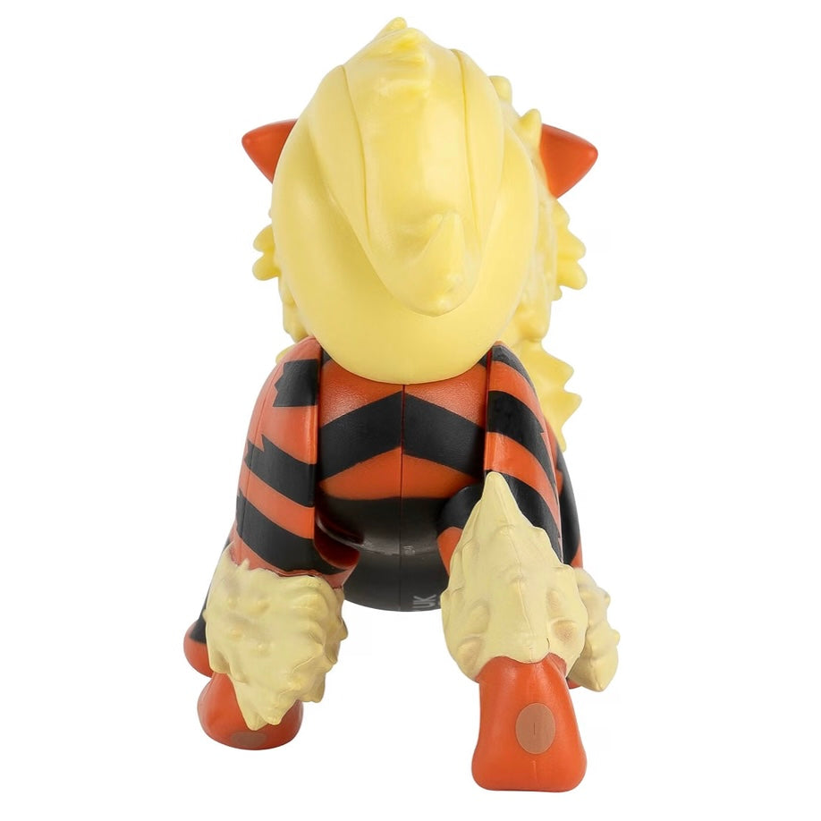 A stylized toy figure resembling a tiger or dragon, shown from the back. The figure has a large yellow head, orange and black striped body, cream-colored paws, and orange feet, photographed against a plain white background.
