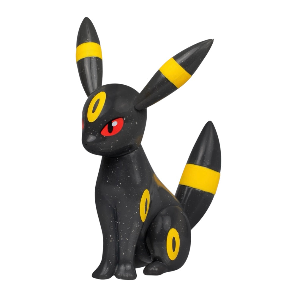 A collectible figurine of Umbreon, a black Pokémon with yellow stripes on its ears and tail and a red eye, shown against a plain white background.