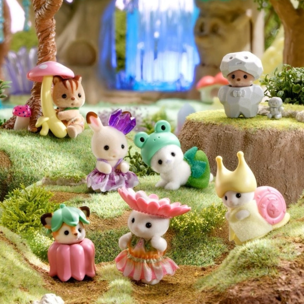 A group of small, cute animal-like toy figurines dressed in colorful fantasy outfits, arranged on a mossy forest floor with trees, flowers, and a waterfall backdrop.